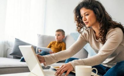 Femme travaillant sur ordinateur portable depuis son domicile, avec un enfant sur son canapé